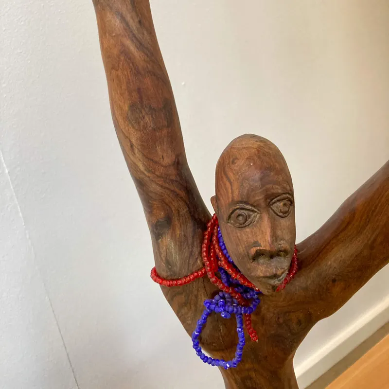 Carved figure with raised arms and beaded necklaces