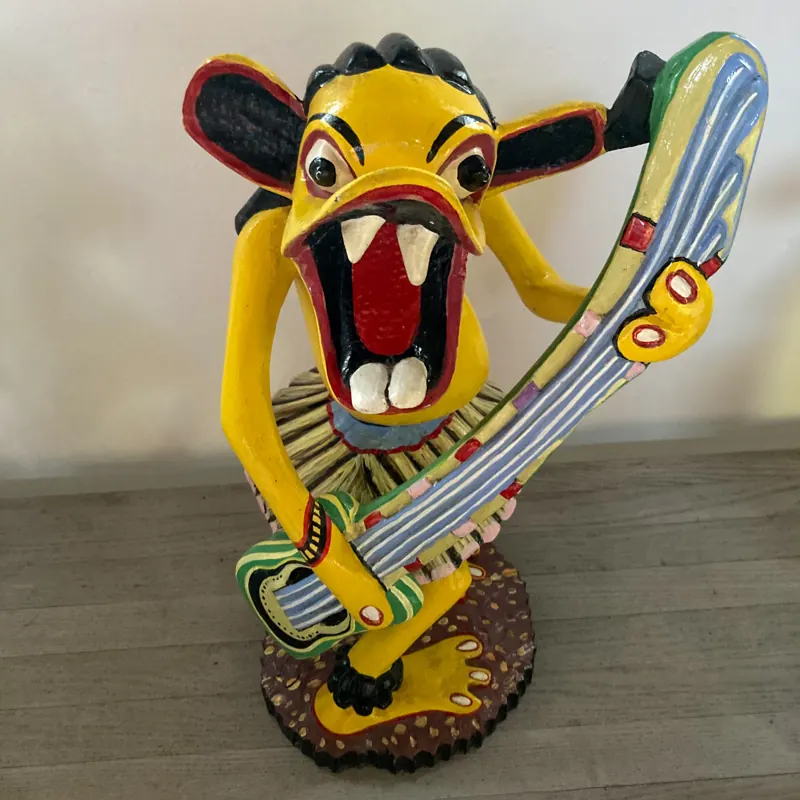 Painted Shetani carving of a yellow creature playing a guitar