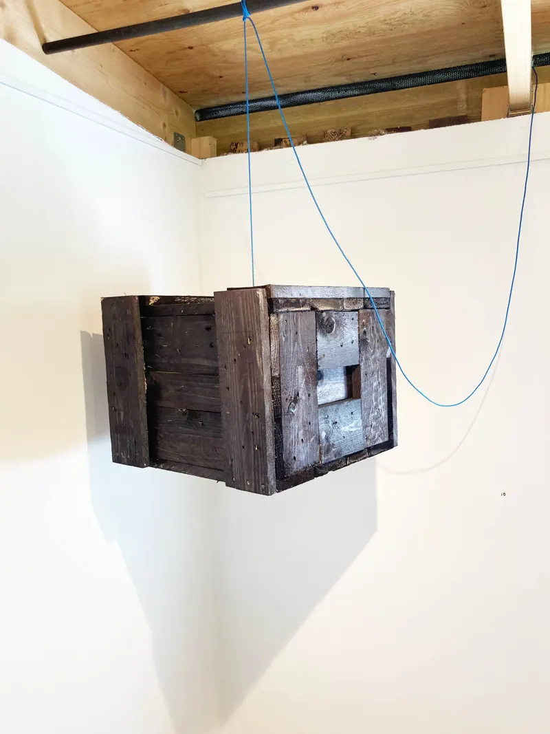 Weathered wooden crate hung on a blue cord in a corner