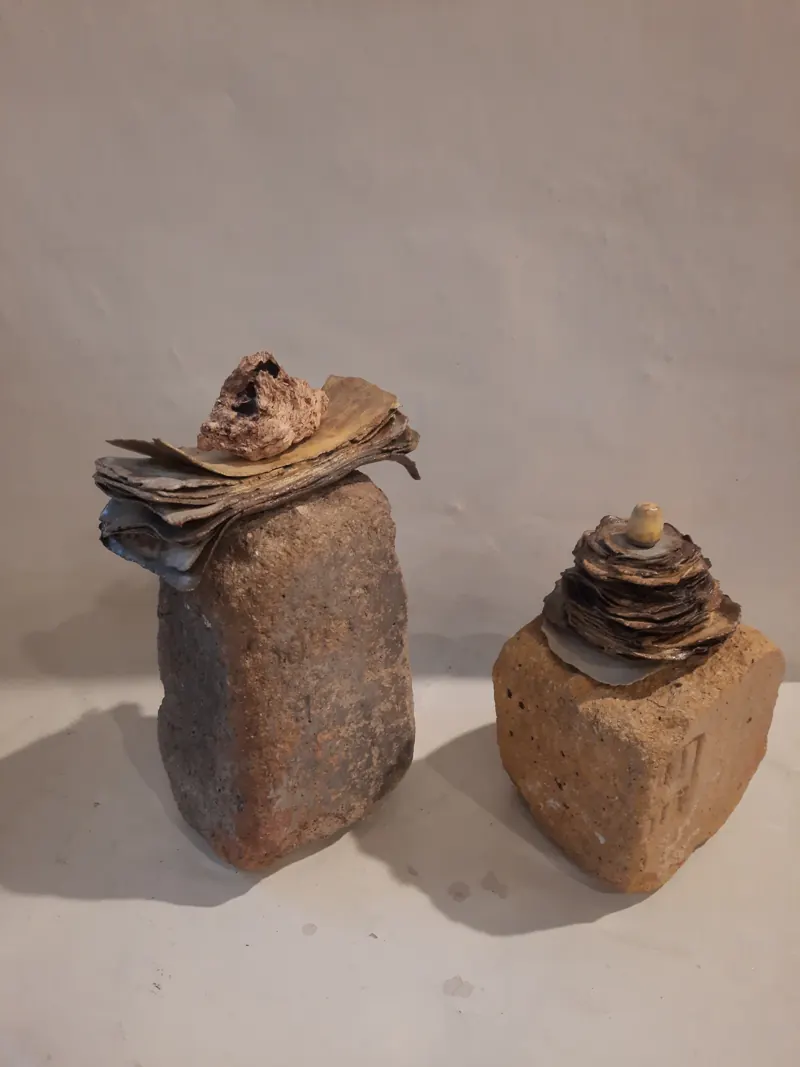 Two ceramic sculptures, rough stone-like blocks topped with layered forms