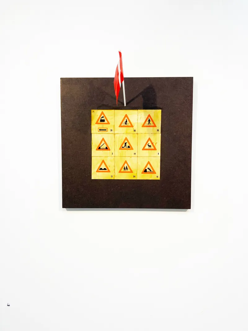 Yellow warning signs arranged in a grid on a dark board, with a Danish flag