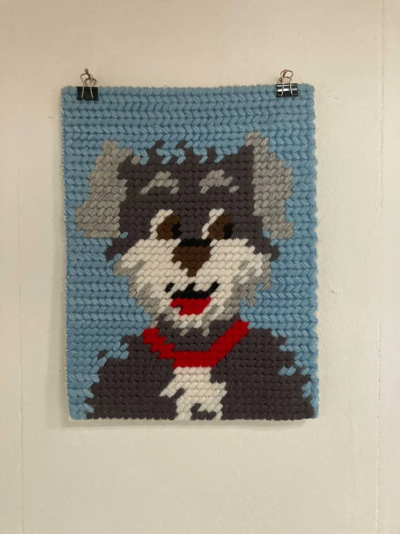 Cross-stitch picture of a grey dog with a red collar