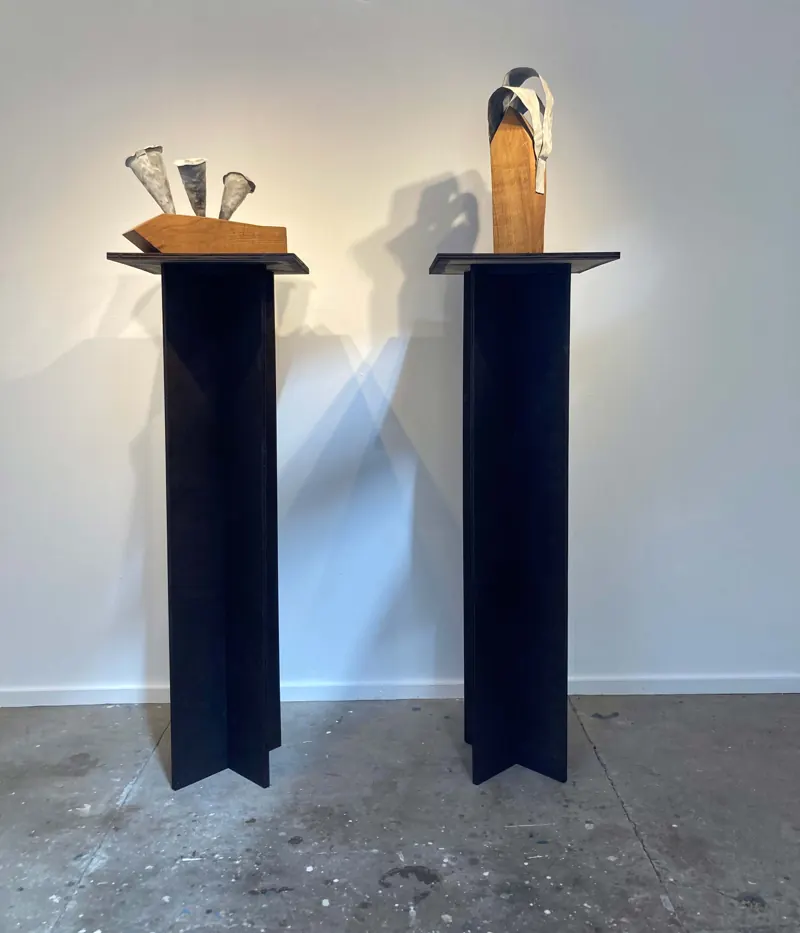 Two carved wooden pieces on tall black steel plinths