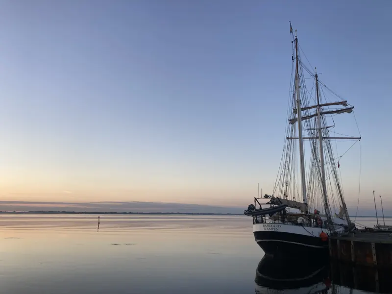 Et stort sejlskib fortøjet i Strynø havn ved daggry, vandet blankt