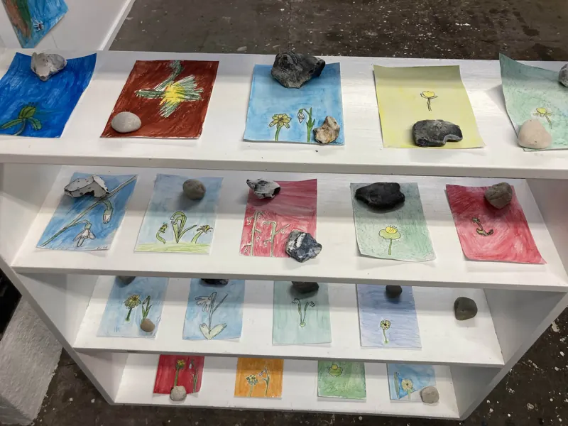Shelves of children’s flower paintings and beach stones