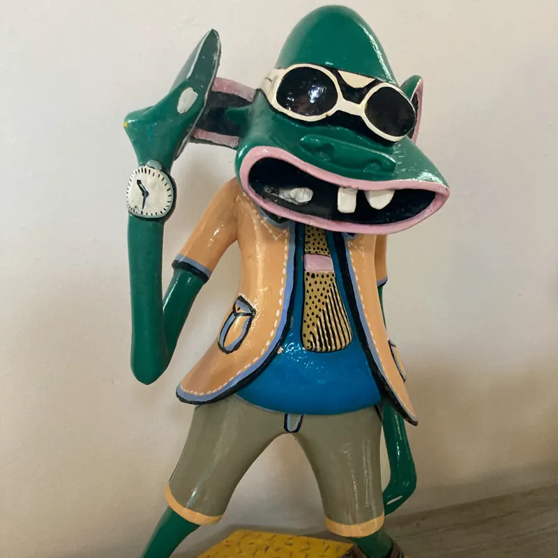 Painted Shetani carving of a green figure in sunglasses