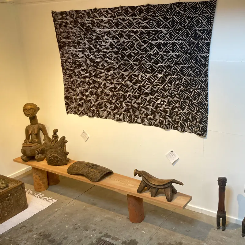 Carvings on a long bench beneath a large Kuba textile