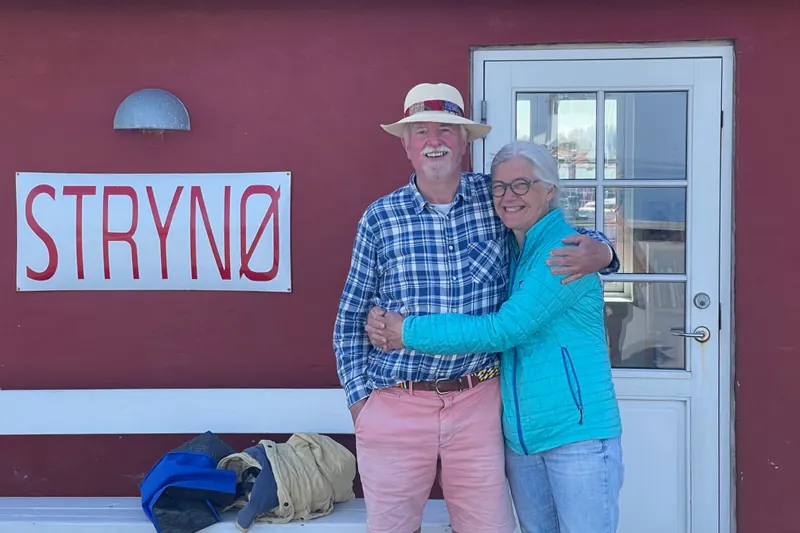 Donna og Jeremy foran en rød bygning med et Strynø-skilt